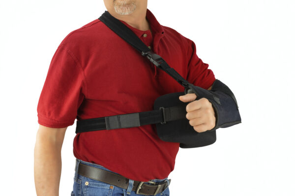 Middle aged man wearing a shoulder surgery sling with abduction pillow to keep his arm in the proper position during recovery and healing after his operation.