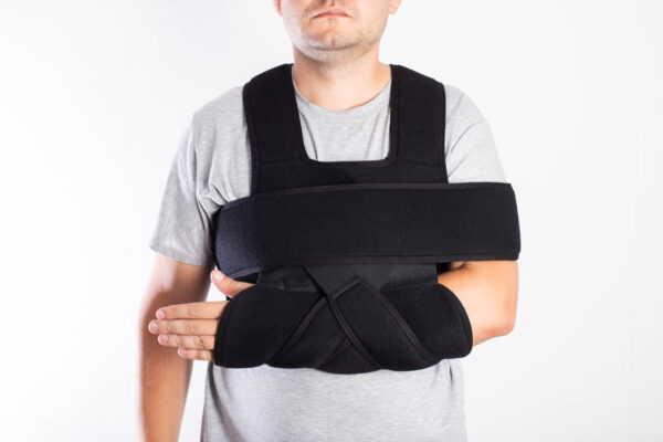 A man in a black bandage supporting the shoulder joint after ligament damage and bruise. Dislocation of the shoulder joint, fracture of the collarbone.